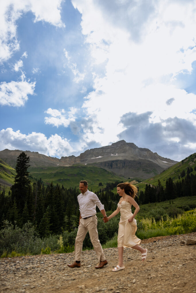 Eloping couple running down a hill in the mountains of Ouray Colorado. 