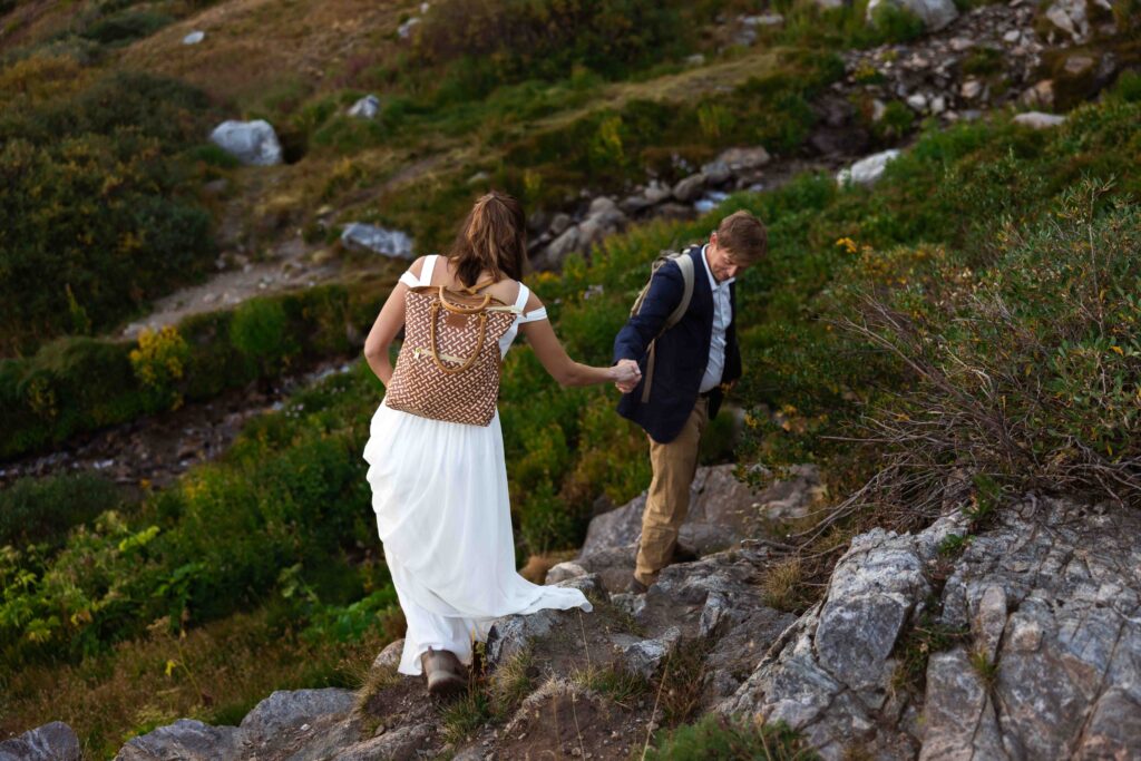 Groom carrying the bride on his back, both laughing as they make their way down the trail.