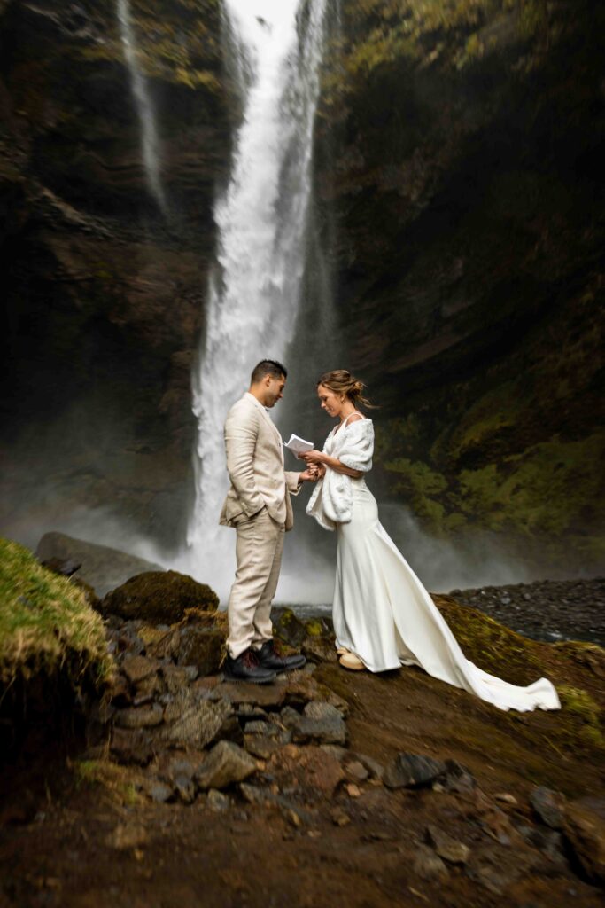 Bride adjusting her veil with the dramatic Icelandic cliffs behind her