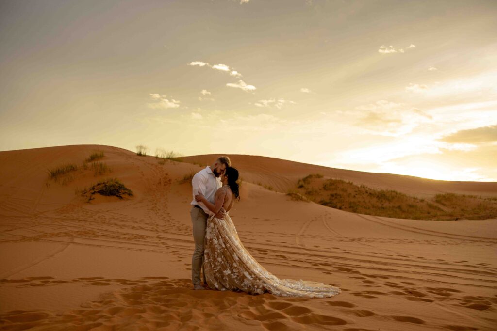 Wide-angle shot of both couples standing atop a sand dune with a vibrant sky behind them