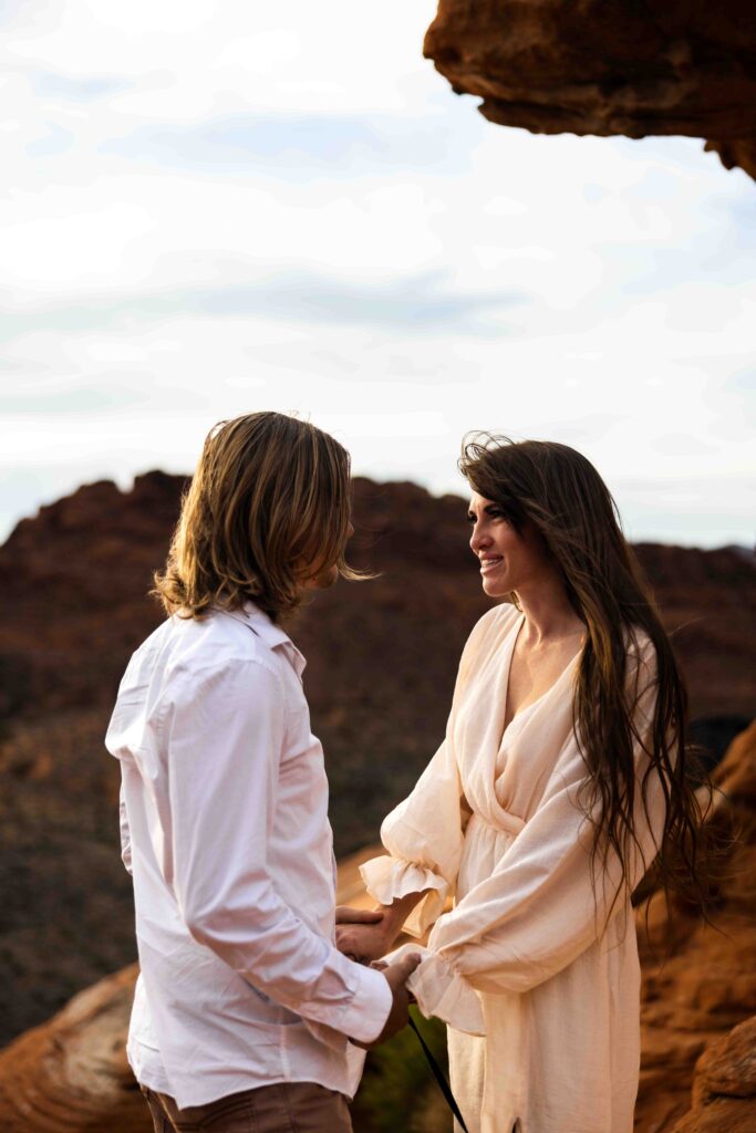 Wide shot of the couple climbing the rock face, with the expansive canyon stretching below them.