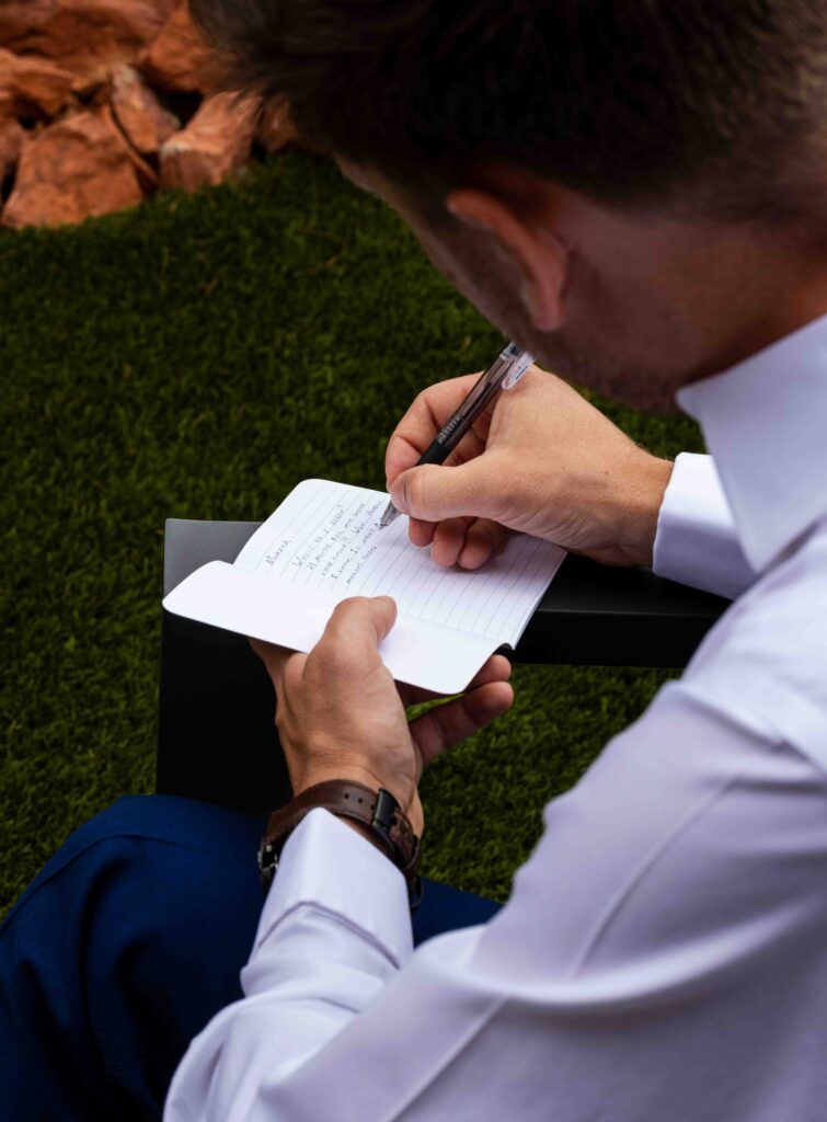 Groom adjusting his tie while looking in a mirror with natural light streaming in
